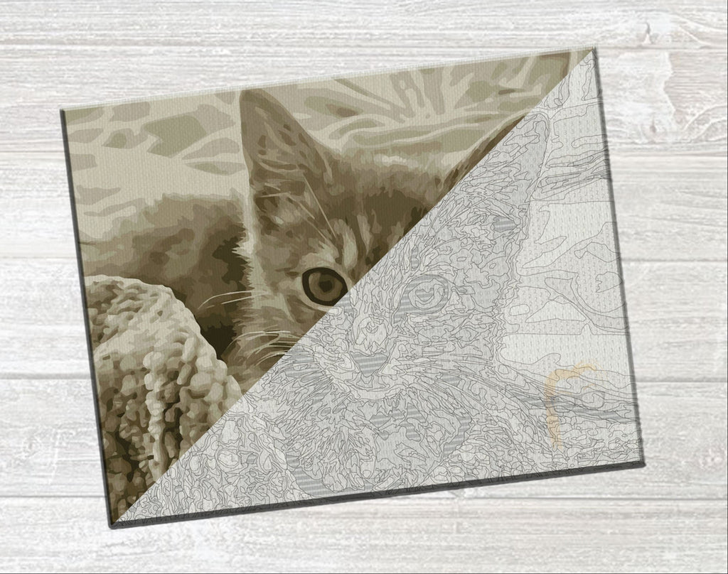 A square canvas art print featuring a sepia-toned kitten peeking from behind a diagonal line of fine line art, displayed on a light gray wood-textured background.